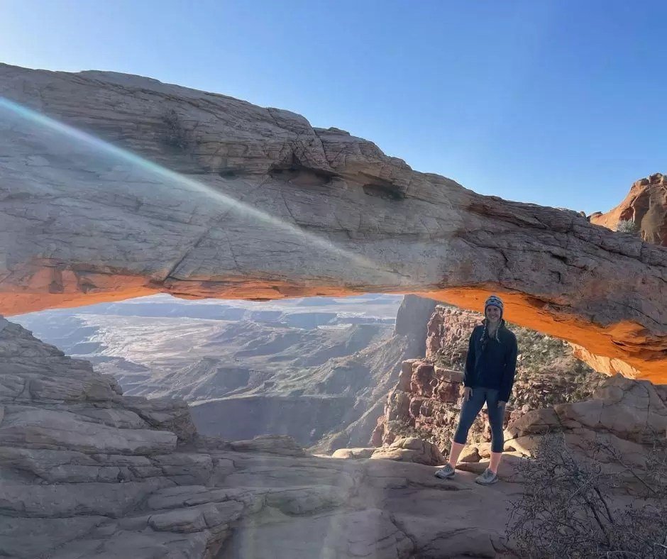 woman standing by mesa arch during early morning dawn hours