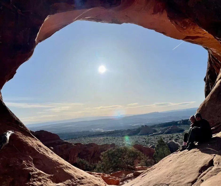 couple sitting at partition arch during sunrise in arches national park