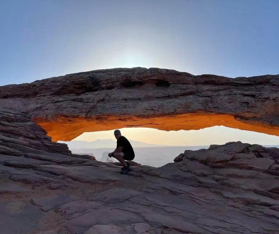 man crouching down under mesa arch sunrise canyonlands national park
