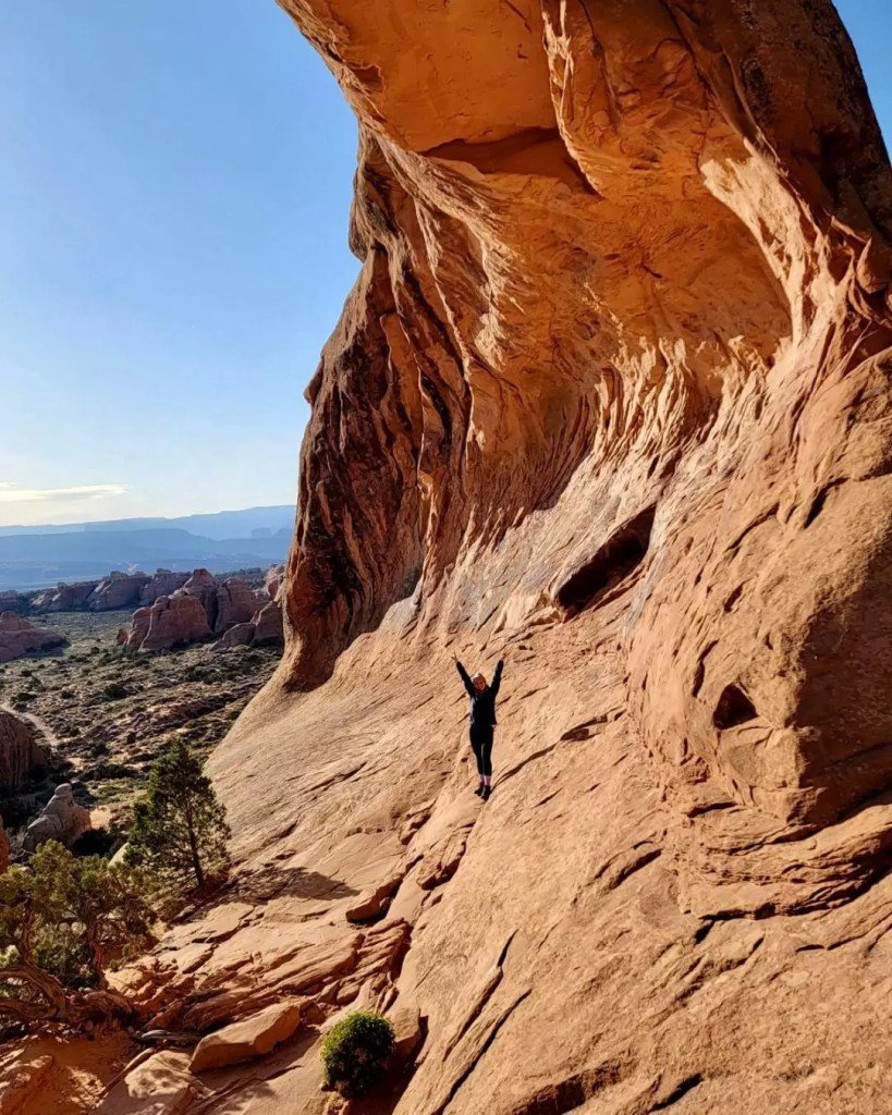 A woman with her arms up while under partition arch on the devils garden trail