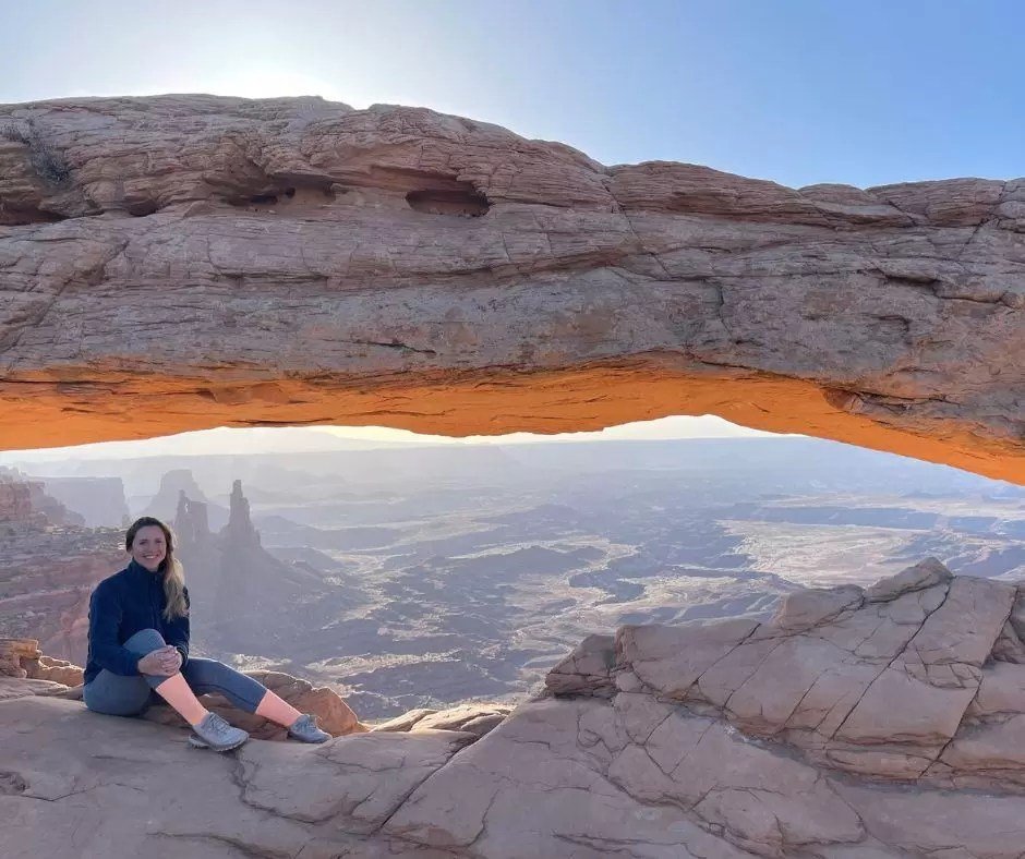 woman sitting under mesa arch at sunrise in canyonlands national park