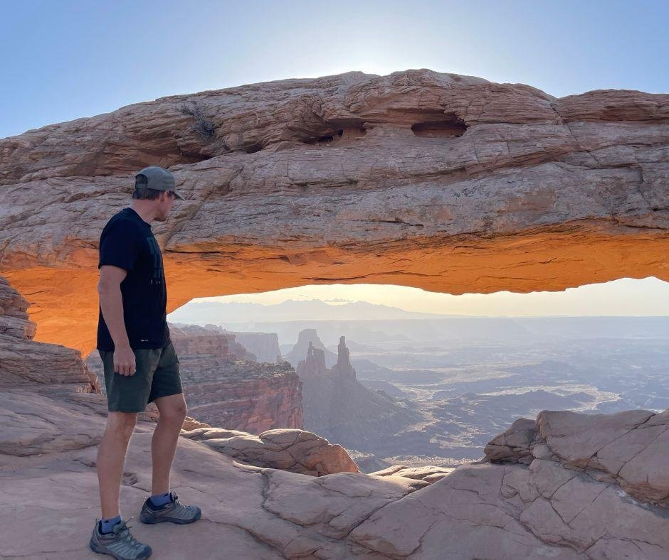 man looking through mesa arch sunrise at canyonlands national park